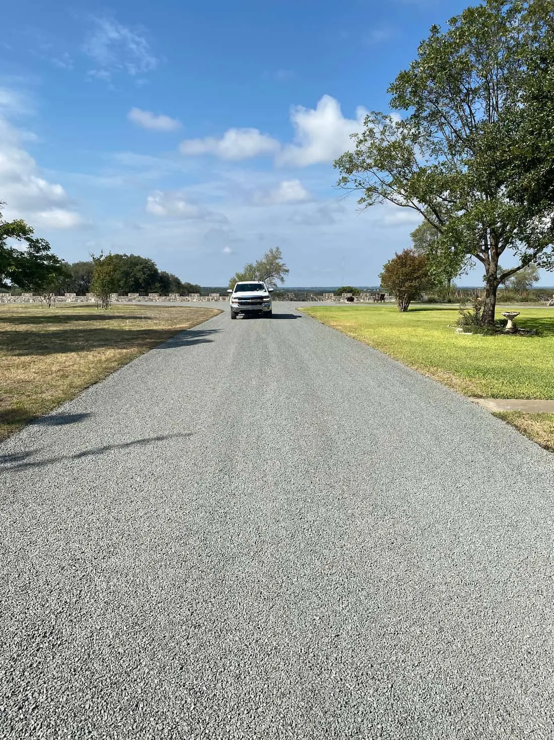 Finished chip seal driveway leading toward a white pickup truck under a blue sky